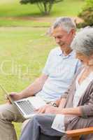 Smiling senior couple using laptop at park