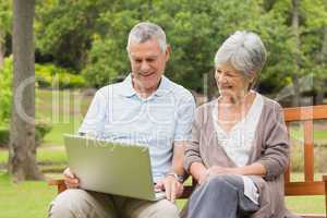 Smiling senior couple using laptop at park