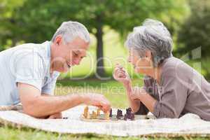 Happy senior couple playing chess at the park