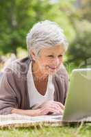 Smiling senior woman using laptop at park