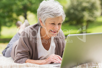 Smiling senior woman using laptop at park