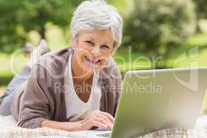 Smiling senior woman using laptop at park