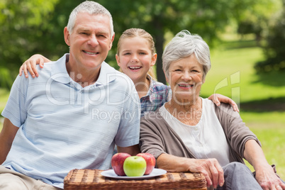 Smiling senior couple and granddaughter with picnic basket at pa