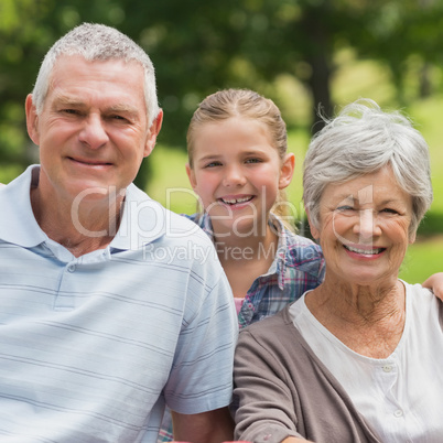 Smiling senior couple and granddaughter at park