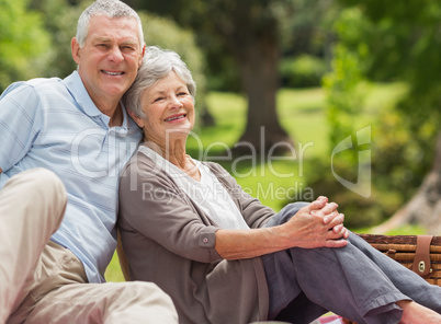 Smiling senior couple sitting with picnic basket at park