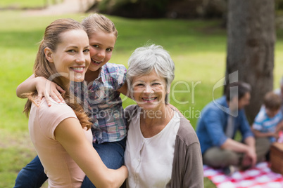 Grandmother, mother and daughter with family in background at pa