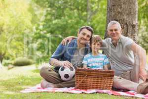 Grandfather, father and son with picnic basket at park