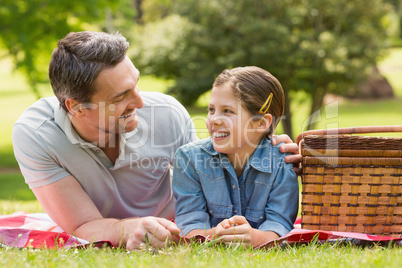 Smiling father with young daughter lying on grass in park