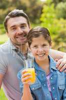 Smiling father with young daughter holding orange juice in park
