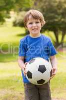 Smiling young boy holding ball in park