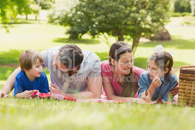 Smiling couple with young kids lying on grass in park