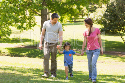 Family of three holding hands and walking at park