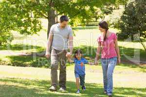 Family of three holding hands and walking at park