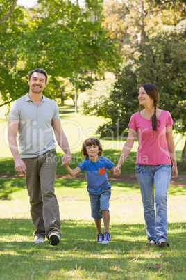 Family of three holding hands and walking at park