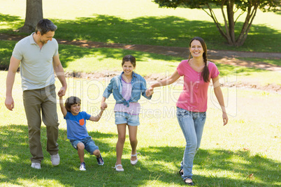 Family of four holding hands and walking at park