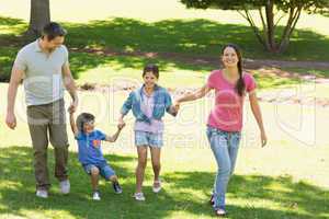 Family of four holding hands and walking at park