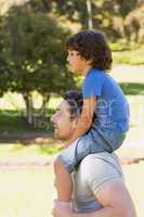Smiling man carrying son on his shoulders in park