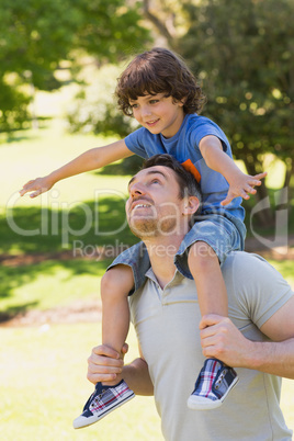 Smiling man carrying son on his shoulders in park