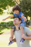 Smiling man carrying son on his shoulders in park