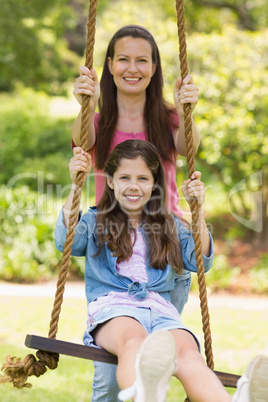 Happy mother pushing daughter on swing