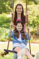 Happy mother pushing daughter on swing