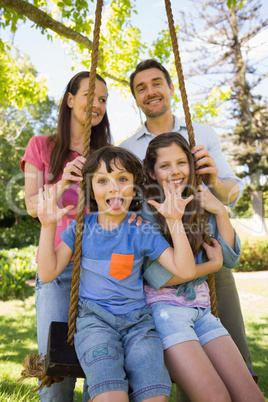 Happy couple pushing kids on swing