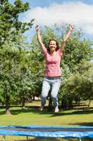 Happy woman jumping high on trampoline in park