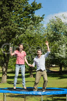 Happy couple jumping high on trampoline in park