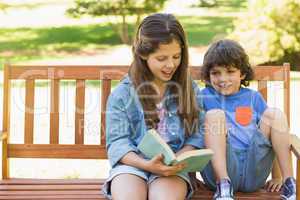 Kids reading book on park bench