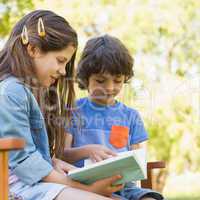 Side view of kids reading book on park bench
