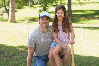 Father and daughter holding baseball bat in park