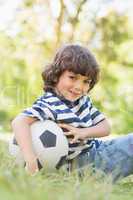 Cute little boy with football sitting on grass in park