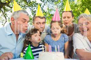 Extended family blowing cake outdoors