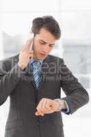 Serious businessman checking the time while on the phone