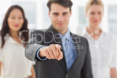 Smiling businessman pointing to camera in front of his team