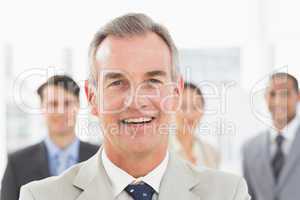 Mature businessman smiling at camera with team behind him