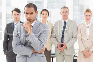 Serious businessman frowning at camera with team behind him