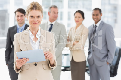 Happy businesswoman using her tablet with team behind her