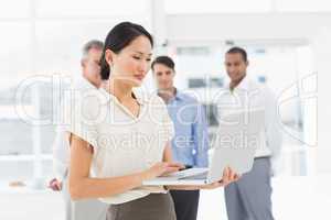 Pretty asian businesswoman using laptop with team behind her