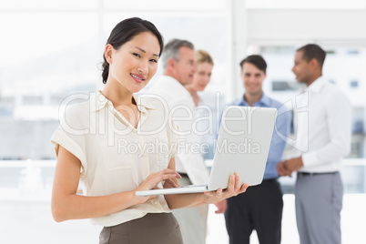 Smiling asian businesswoman using laptop with team behind her