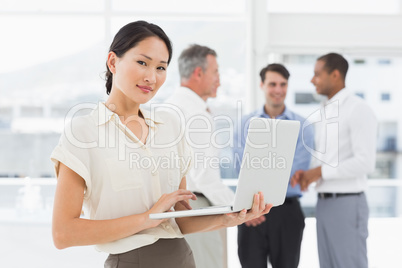 Asian businesswoman using laptop with team behind her