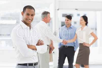 Young businessman with team behind him smiling at camera