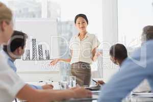 Smiling asian businesswoman presenting bar chart to colleagues