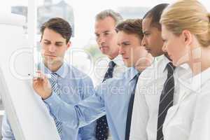 Colleagues watching young businessman write on whiteboard