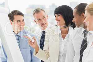 Colleagues watching happy businesswoman pointing to whiteboard