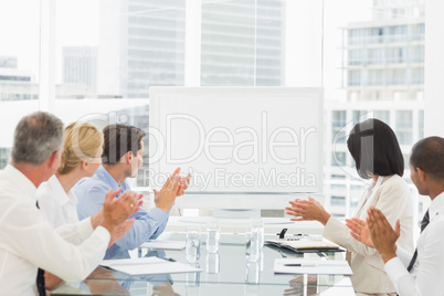 Business people applauding blank whiteboard in conference room