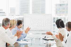 Business people applauding blank whiteboard in conference room