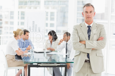 Serious businessman looking at camera while staff discuss behind