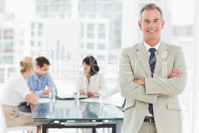 Happy businessman looking at camera while staff discuss behind h