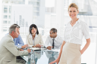 Happy businesswoman looking at camera while staff discuss behind